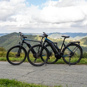 Twee e-MTB's geparkeerd op uitkijkpunt met groene Alta Langa heuvels op de achtergrond