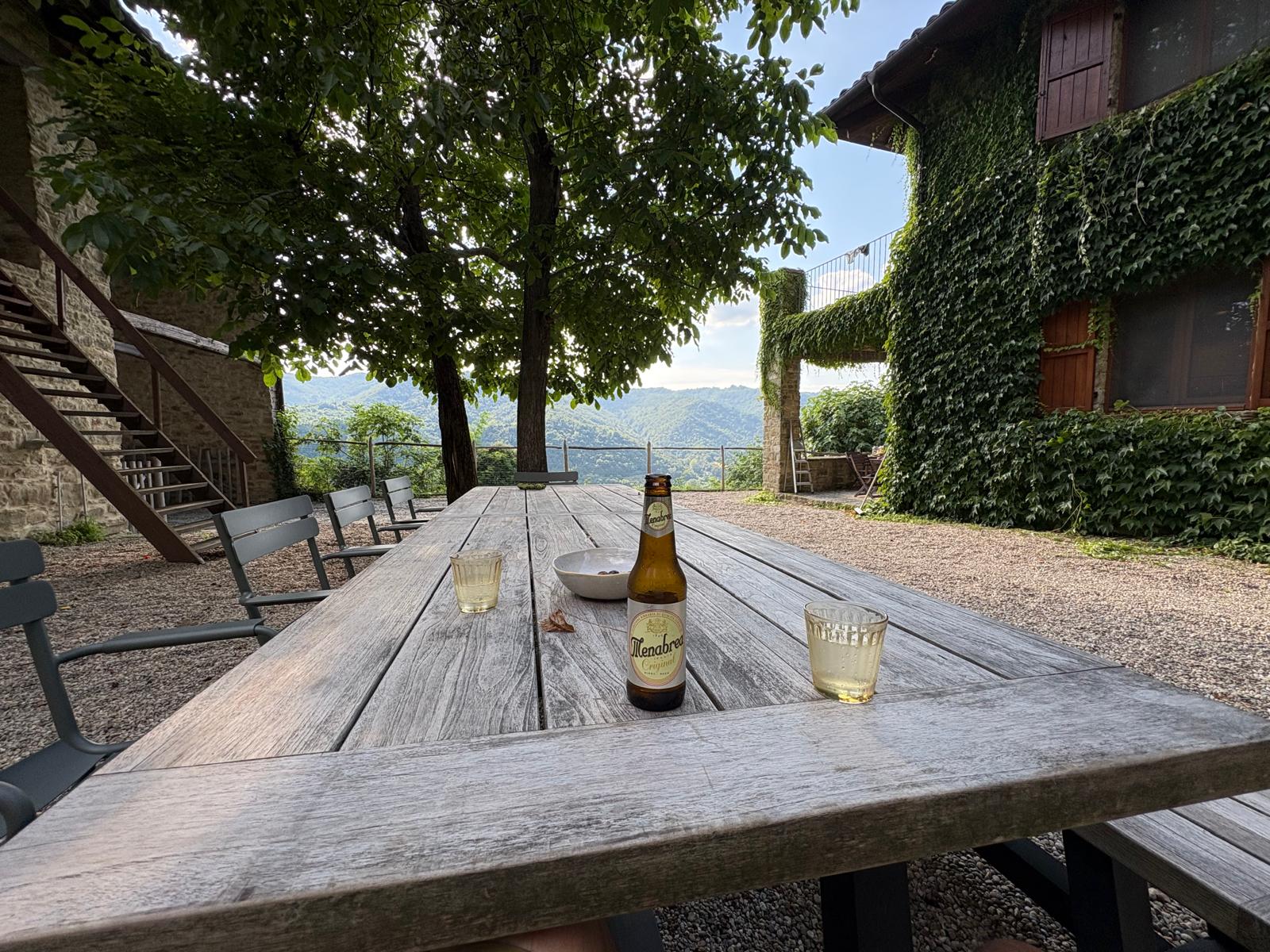 Terras met lange houten tafel en biertje onder de bomen